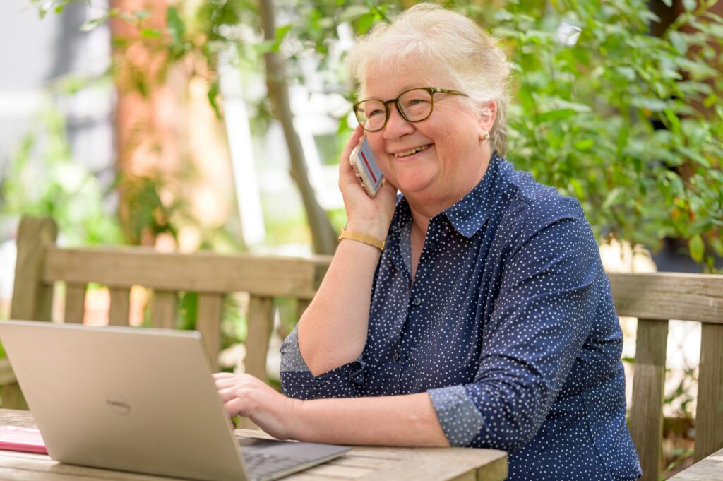Äldre kvinna som pratar i telefon och använder en bärbar dator